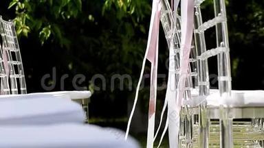 白色和粉红色的丝带在椅子上飘扬。 结婚典礼。 透明椅子